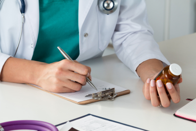 Close-up view of female doctor hand holding bottle with pills and writing prescription. Healthcare, medical and pharmacy concept.